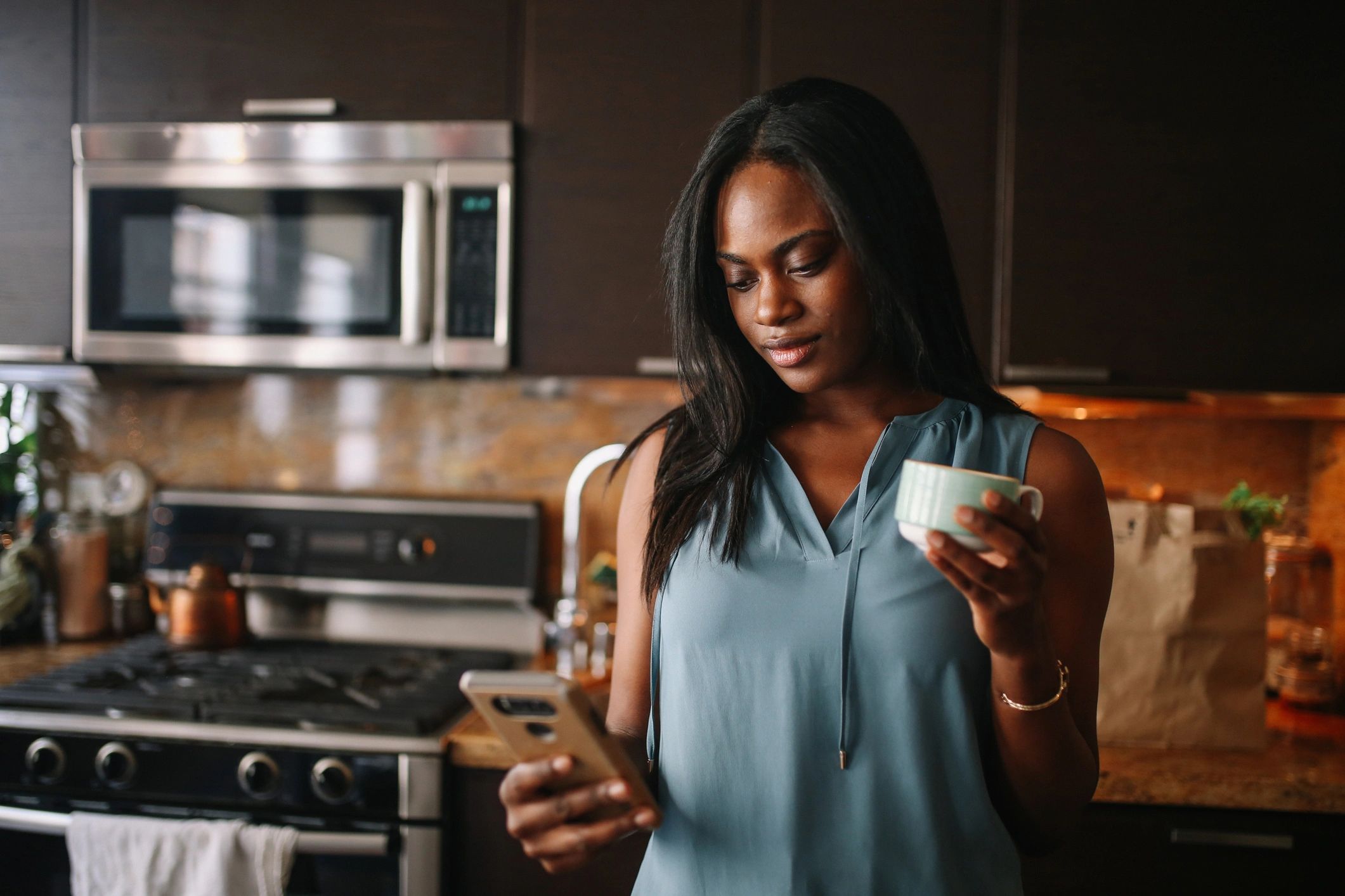 Woman at home reviewing information on her phone with a cup of coffee